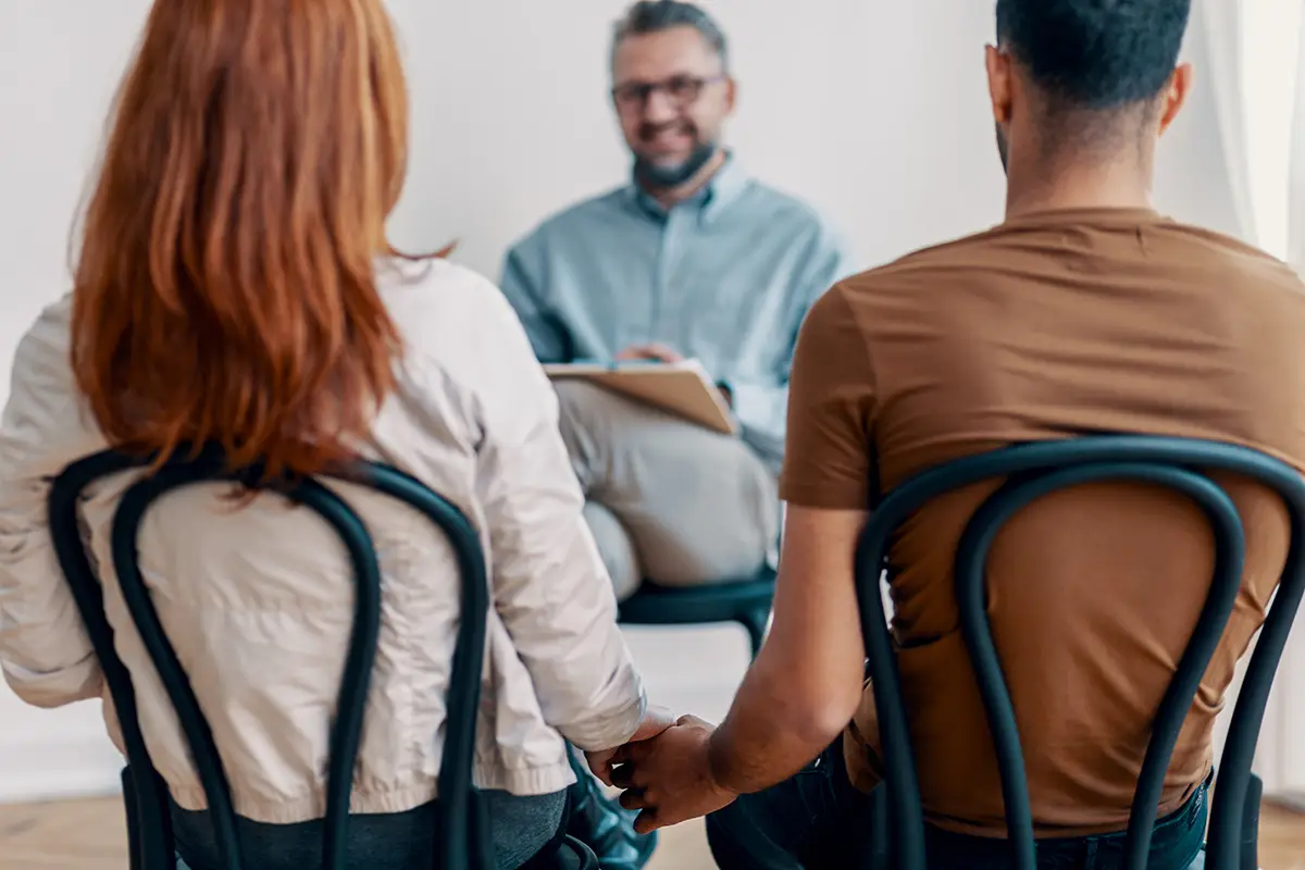 Couple holding hands during a couples counseling session with a therapist seated across from them.